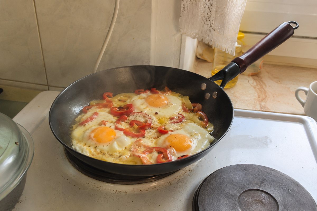 Cast-iron pan with eggs and peppers on the stove